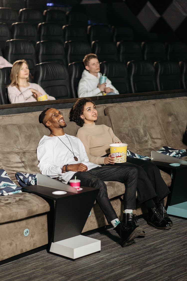 A Couple Sitting On A Couch In A Movie Theater