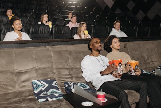 Audience watching a movie with popcorn in a cozy theater setting, diverse group.
