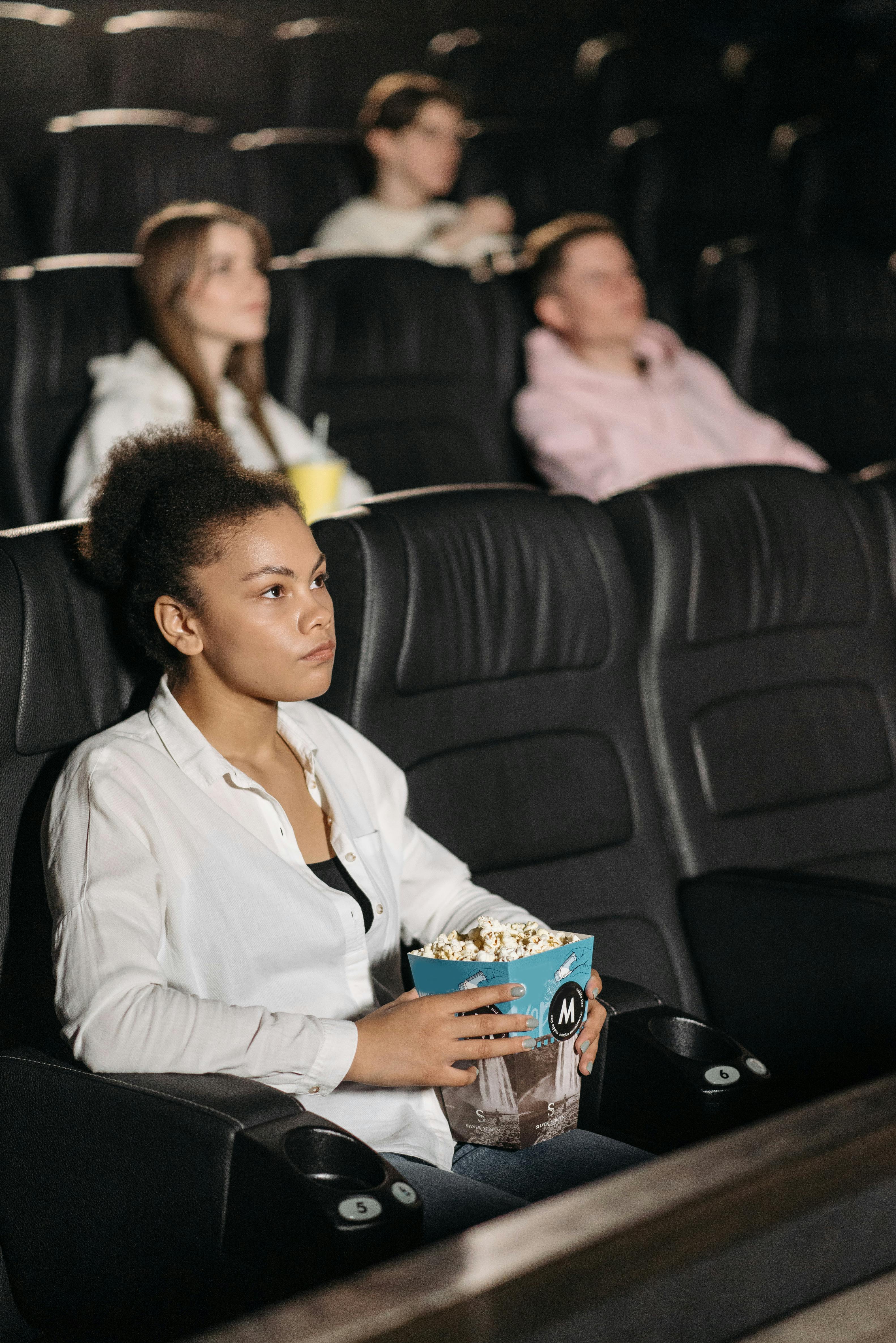 woman in a white shirt holding a bucket of popcorn in a movie theater