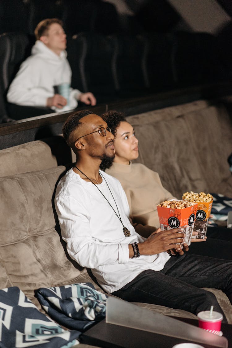 Selective Focus Photo Of A Couple Holding Buckets Of Popcorn While Watching A Movie