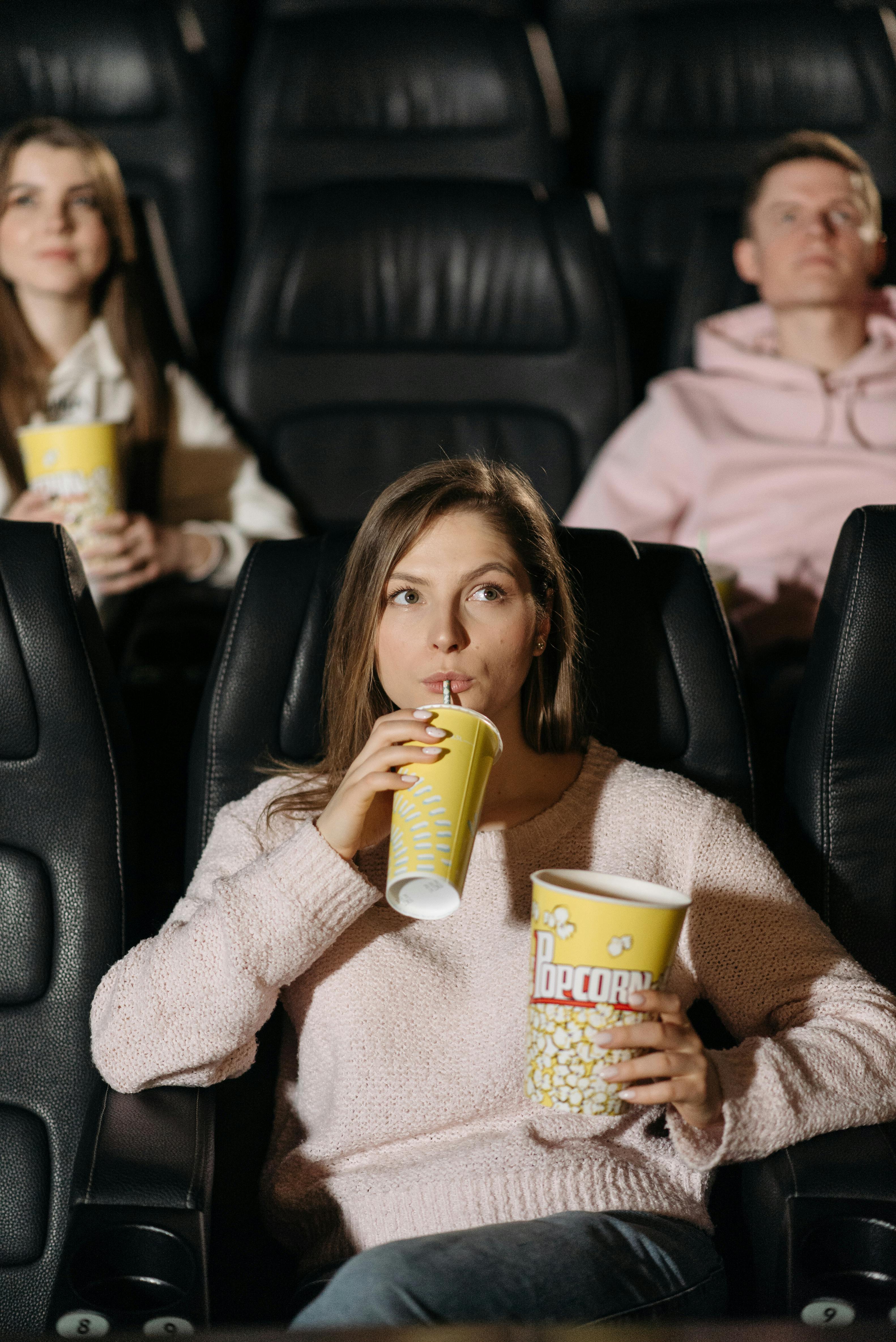 girl in a pink sweater drinking on yellow cup while watching a movie