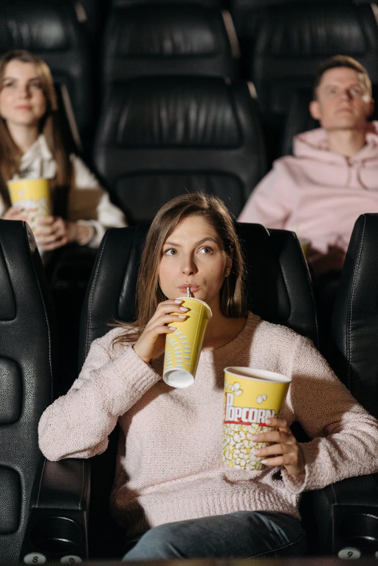 Girl In A Pink Sweater Drinking On Yellow Cup While Watching A Movie