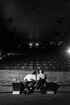 Black and white photo of a couple relaxing in an empty cinema, creating an intimate movie night ambiance.