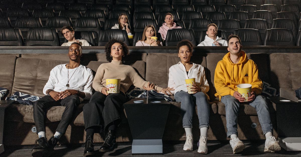 A group of friends watching a live interactive movie on a large screen, with voting buttons visible on their phones