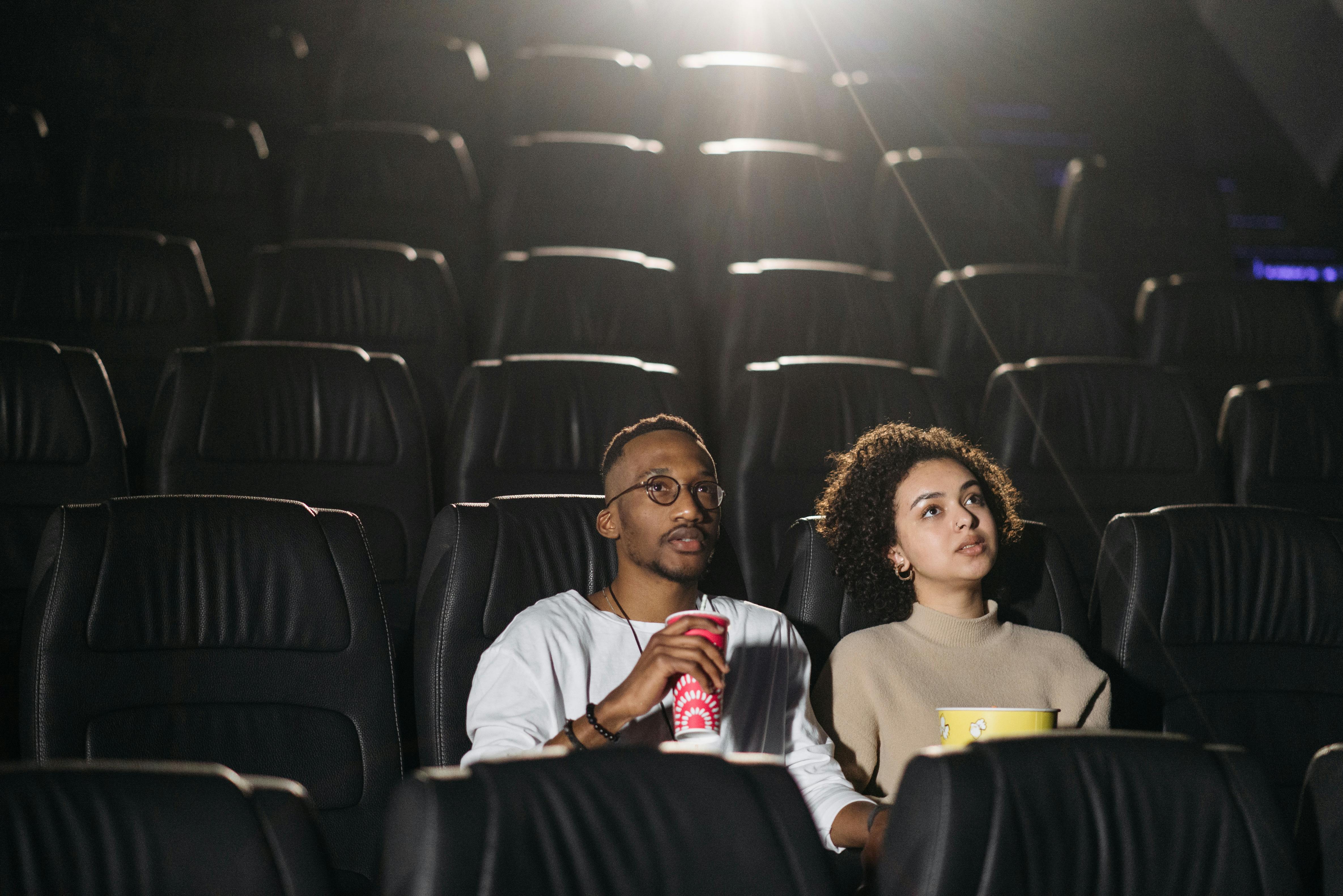 Free A couple seated in a movie theater enjoying a film together with snacks. Stock Photo