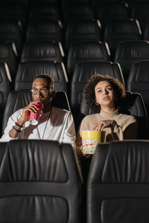 Free Young couple sitting in a movie theater, enjoying popcorn and drinks while watching a film. Stock Photo