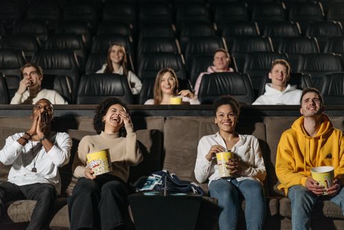 Free A diverse group of friends laughing and enjoying popcorn in a movie theater. Stock Photo
