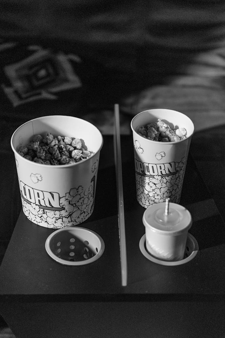 A Bucket And Tumbler Of Popcorns Beside A Cup Of Beverage