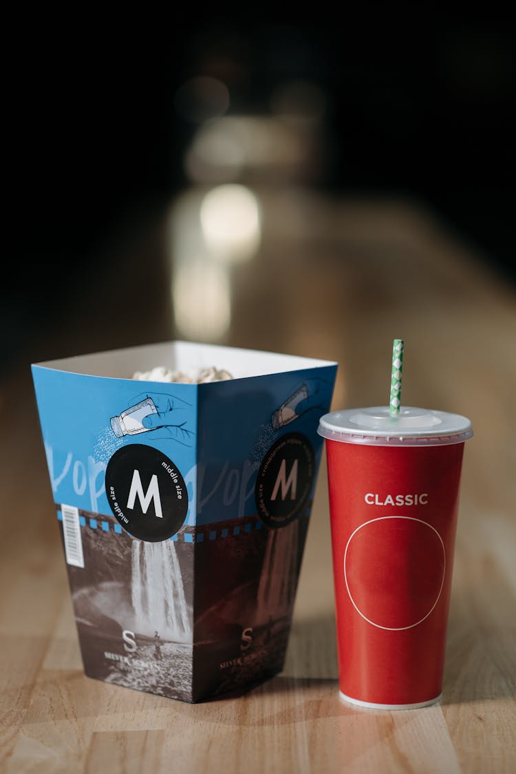 A Paper Tumbler Beside A Red Disposable Cup With Straw