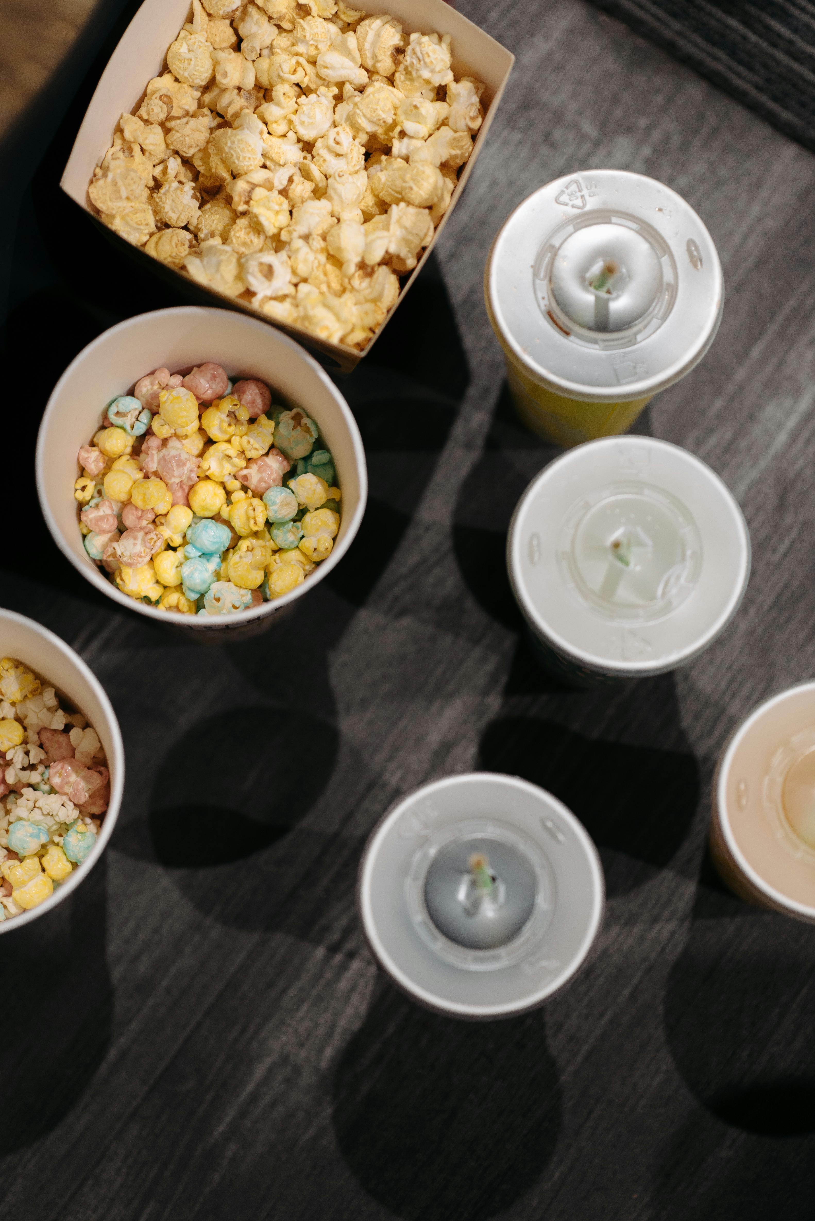Free A flat lay image of colorful popcorn and drinks with lids, perfect for a movie night theme. Stock Photo