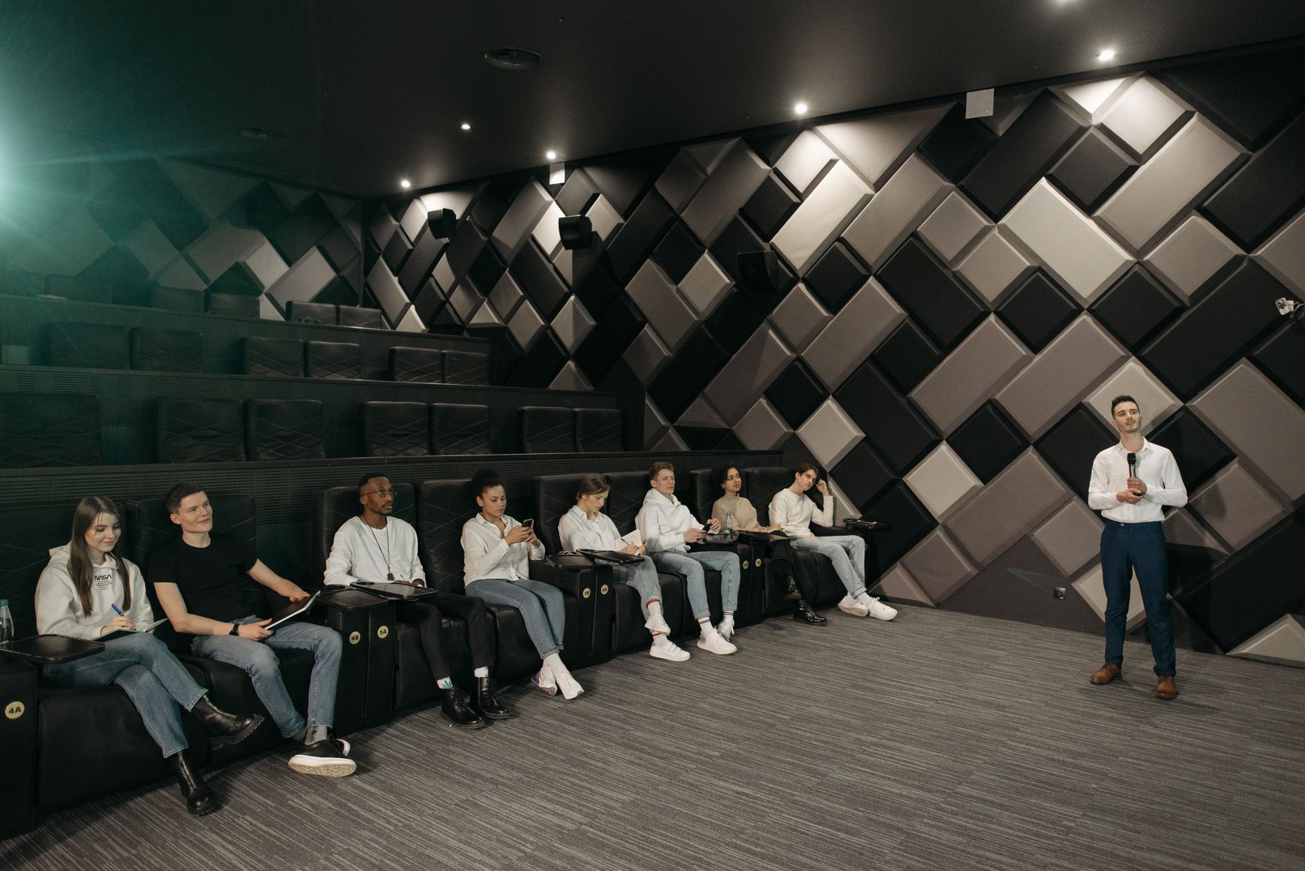 Speaker addressing a diverse audience in a modern theater setting.