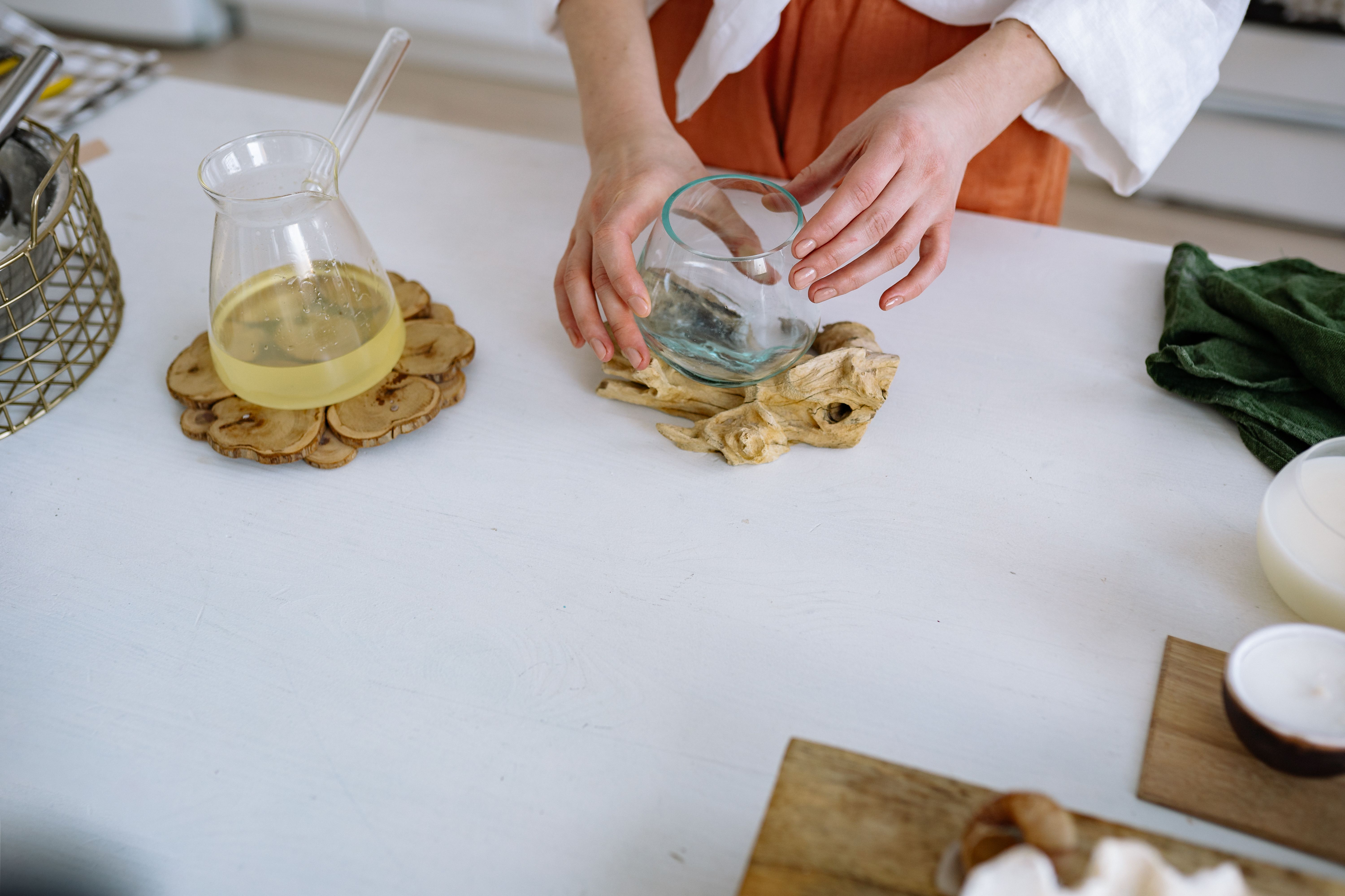 Hands arranging glassware on a wooden coaster on a minimal kitchen countertop