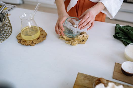 Hands arranging glassware on a wooden coaster on a minimal kitchen countertop.