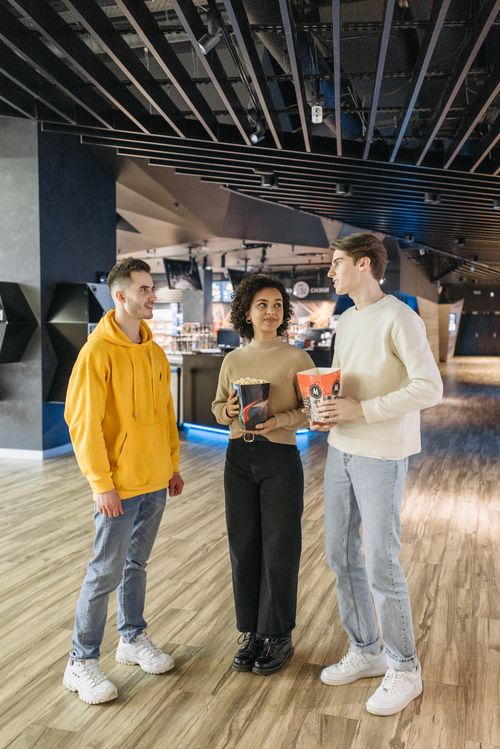 Free Three friends enjoying time together with popcorn at a modern cinema setting. Stock Photo