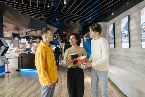 Free A group of friends enjoying popcorn and conversation in a modern cinema hallway. Stock Photo