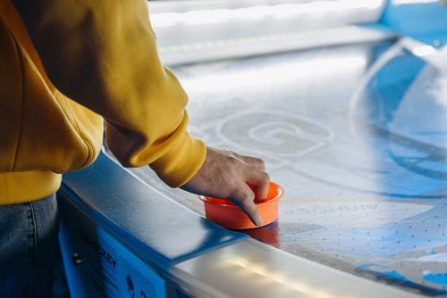 Free Person playing air hockey with an orange paddle at an arcade. Close-up view. Stock Photo