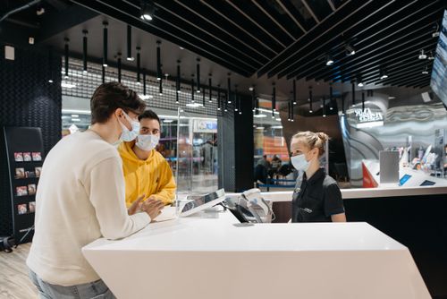 Free Two masked customers at a modern store counter interacting with a masked female staff member. Stock Photo