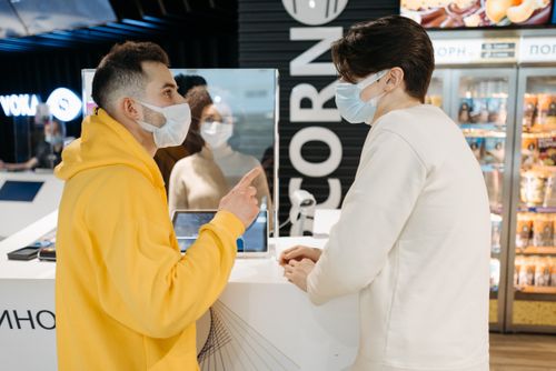 Free Two adults wearing masks having a conversation at a public counter indoors. Stock Photo