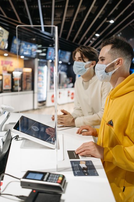 Two masked men using a payment terminal at a counter indoors, following new normal protocols. Two masked men using a payment terminal at a counter indoors, following new normal protocols.