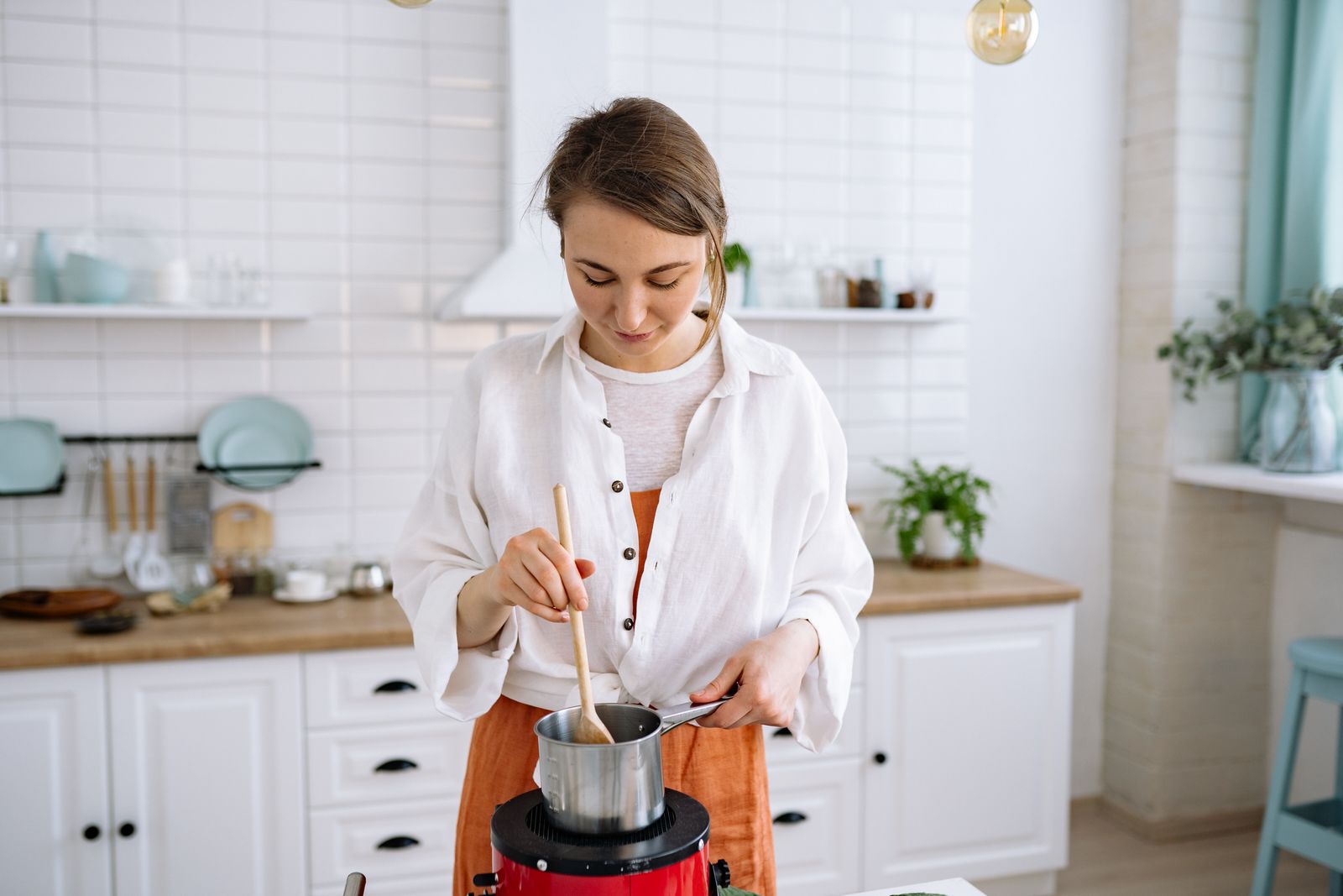 Young woman stirring pot in bright kitchen setting with wooden spoon.