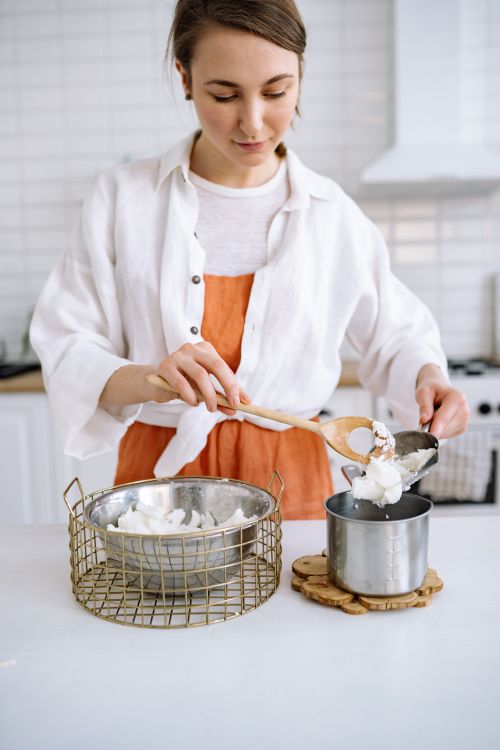 Free Young woman creating handmade candles with wax in a cozy kitchen setting. Stock Photo