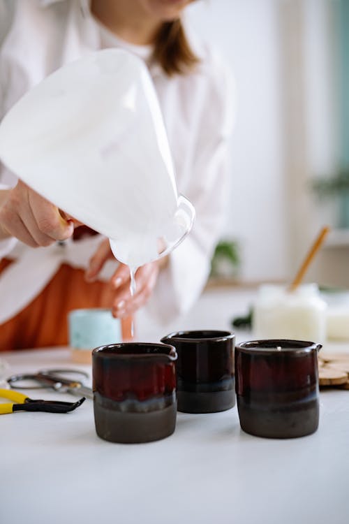 Person Pouring Candle Wax on Ceramic Mugs
