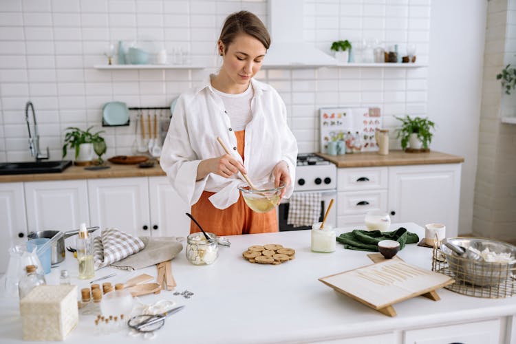 A Woman In Kitchen Holding A Wooden Spatula And A Glass Bowl 