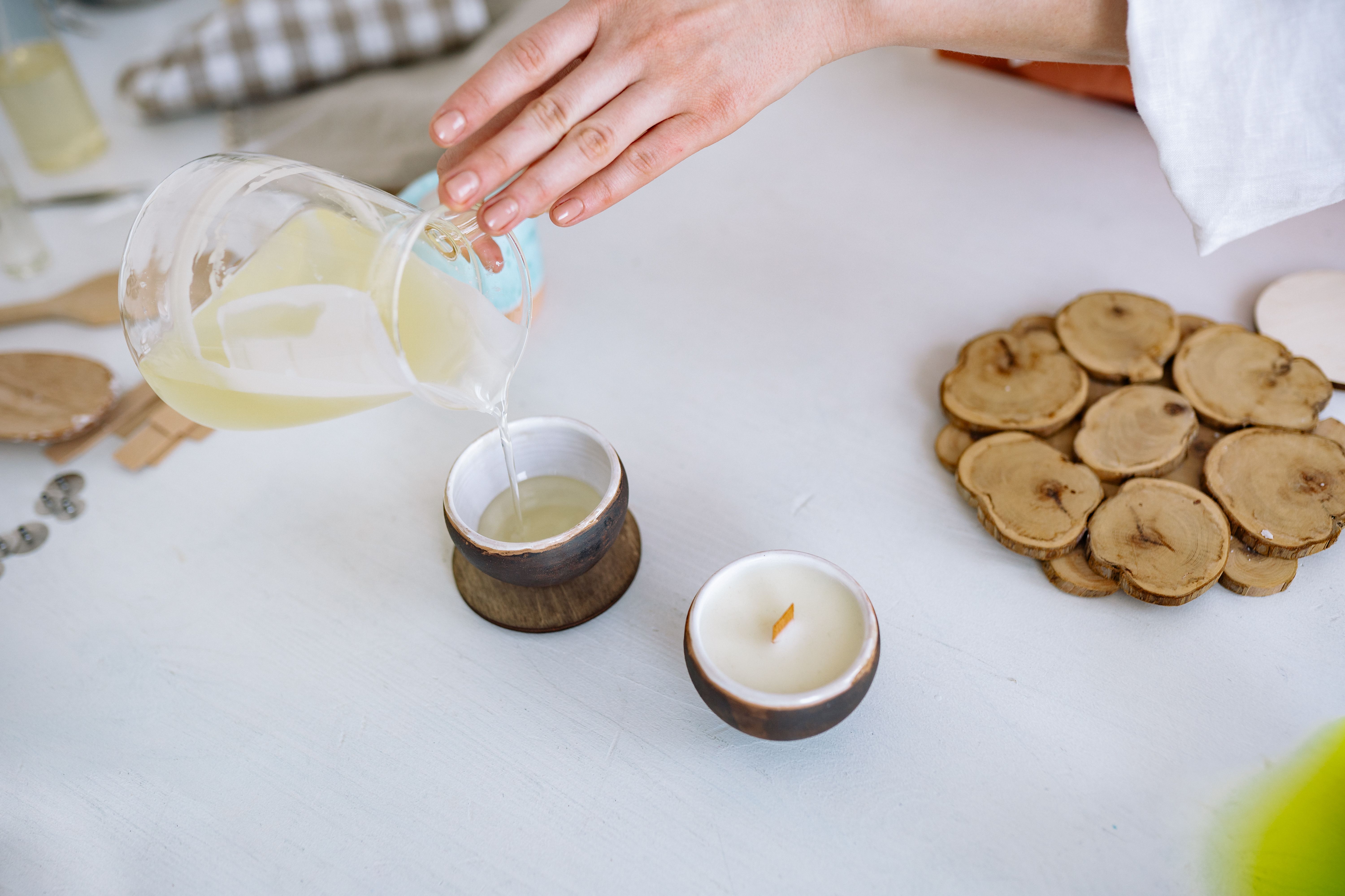 Close-up of hand pouring candle wax into rustic container, crafting essentials nearby.