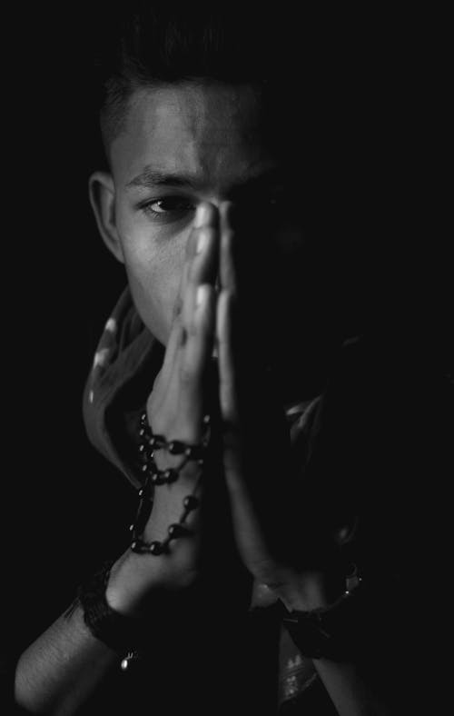 Black and white of ethnic male with rosary beads looking at camera on black background