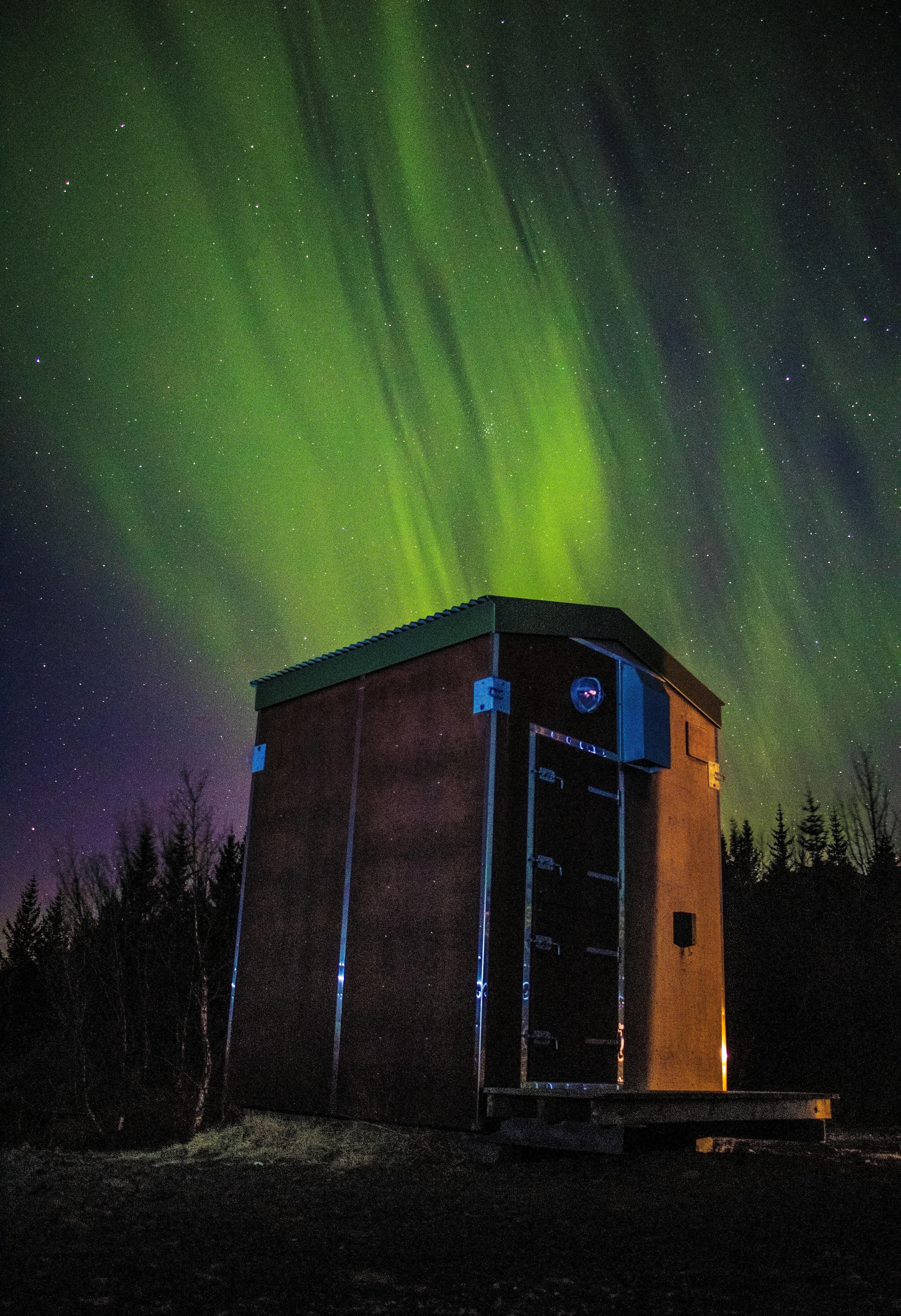 在充满活力的北极光下，宁静的夜空中有一座木屋