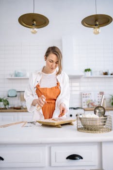 A woman in an orange apron prepares food in a bright, minimalist kitchen.