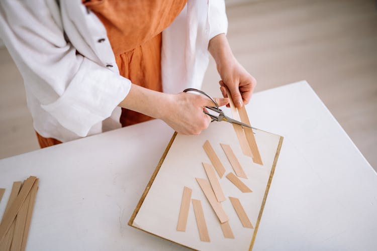 A Person Cutting Wooden Strips With A Pair Of Scissors
