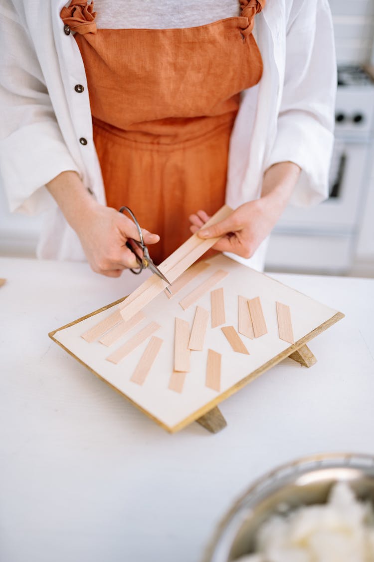 A Person In Orange And White Clothing Cutting Wooden Strips