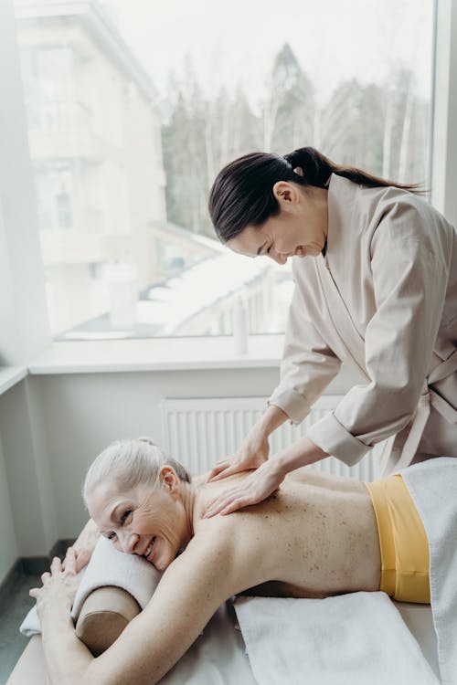 Photo of a Masseuse Massaging an Elderly Woman while Smiling