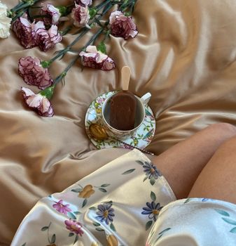Cozy morning vibe with a coffee cup and flowers on a silk bedspread in Tbilisi, Georgia.