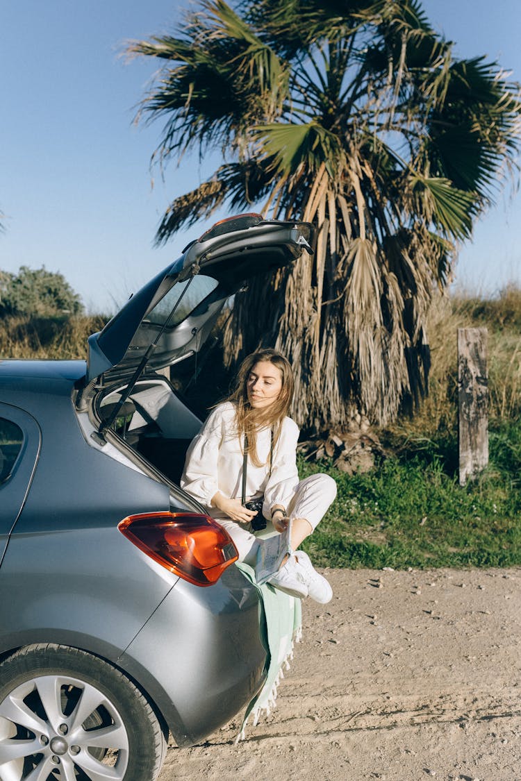 Woman Sitting On The Car Trunk Holding A Camera