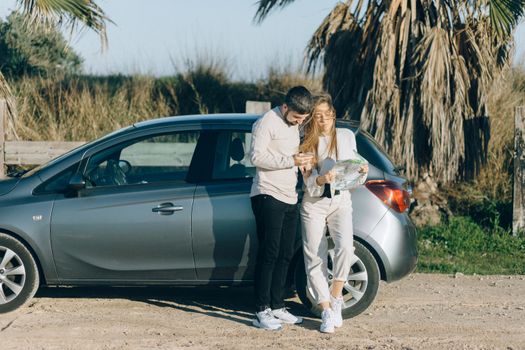 A couple standing by a car using a map to navigate during a sunny road trip.