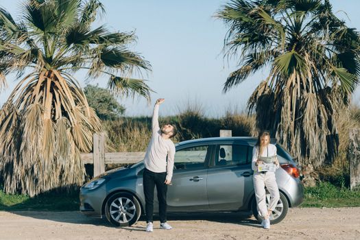 Couple on a road trip using a map near a car by palm trees on a sunny day.