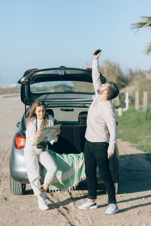 Free A couple enjoys a road trip, checking a map and raising a cellphone for connectivity outdoors. Stock Photo