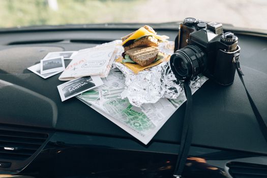 Capture of travel preparation with camera, map, and sandwich on car dashboard.