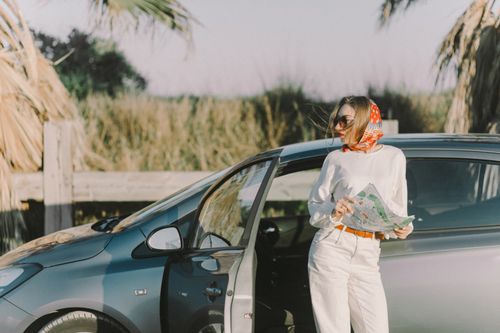 Free Woman with sunglasses and scarf holding a map by car. Perfect for travel and tourism themes. Stock Photo