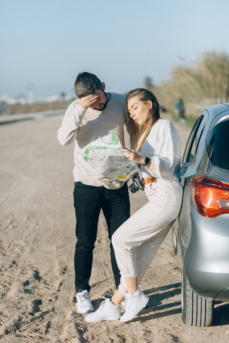 A Man And A Woman Looking At A Map While Outside Their Car