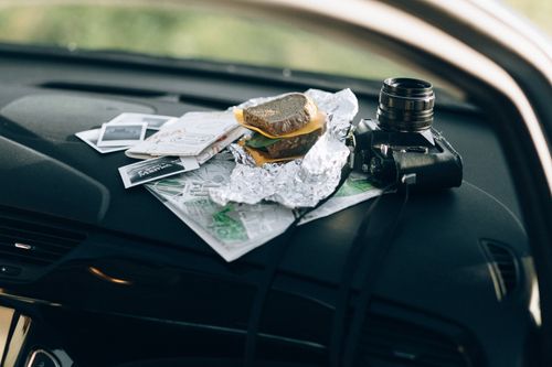 Free A camera and a sandwich wrapped in foil placed on a car dashboard with maps and photos. Stock Photo