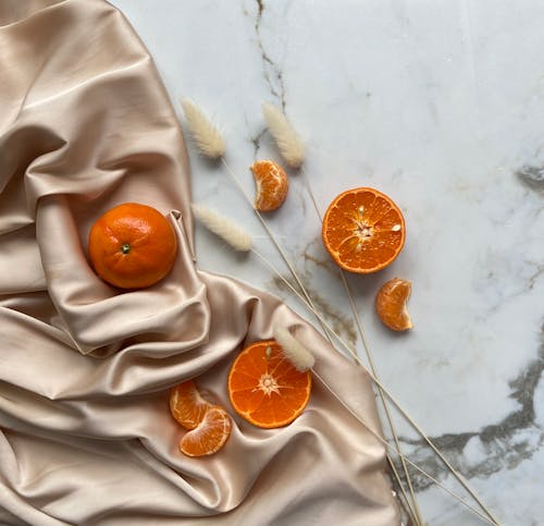 Top view of fresh ripe slices of tangerine and oranges placed on crumpled fabric on marble surface with dried branches