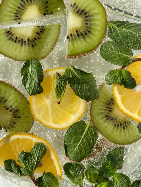 Top view of transparent sparkling beverage with sliced ripe kiwi and sour lemon decorated with fresh aromatic leaves of mint