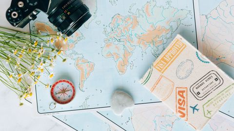 Flat lay of travel essentials: maps, camera, compass, and travel journal for planning adventures.