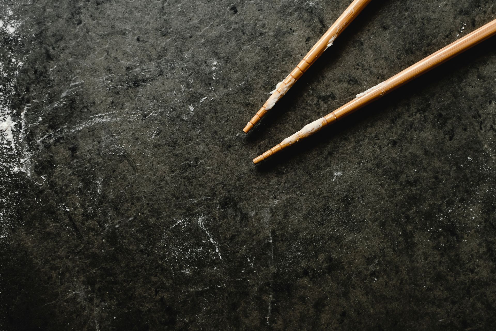 Wooden chopsticks on a dark, flour-dusted surface, close-up view.