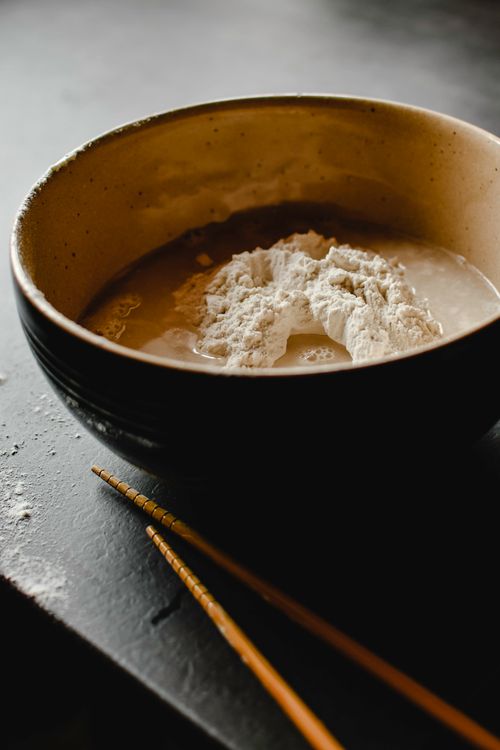 Free Close-up of a rustic bowl with flour and water, paired with chopsticks, suggesting food preparation. Stock Photo