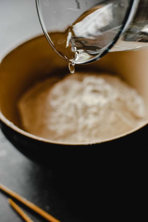 Free Water being poured into a bowl of flour, focusing on food preparation process. Stock Photo
