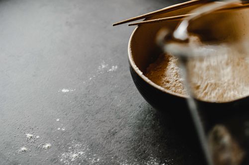 Free Close-up of a bowl filled with flour and chopsticks on a textured gray surface, suggesting a food prep setting. Stock Photo